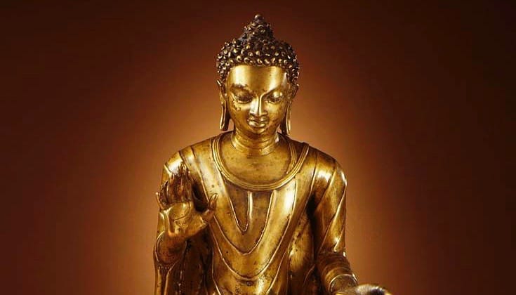 Buddha Shakyamuni statue. It is gold against a brown background.