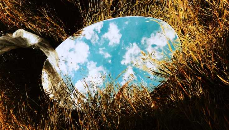 Mirror in tall grass reflecting the sky.