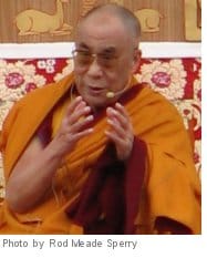 Dalai Lama. He is wearing orange robes and speaking into a microphone.