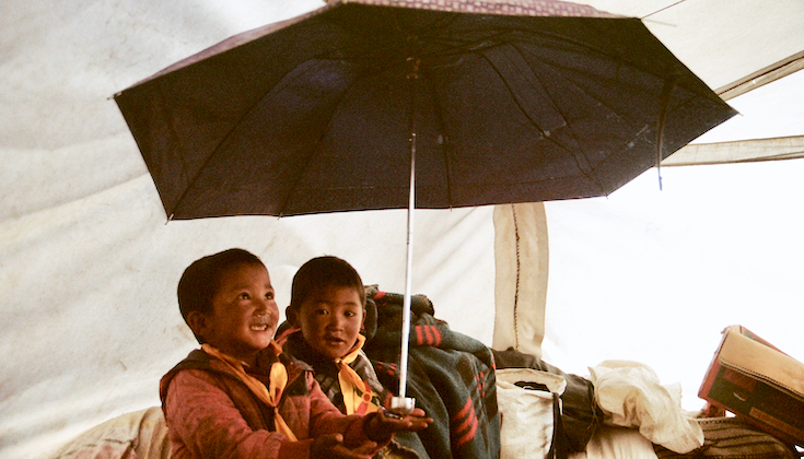 Two third-generation Tibetan refugees play with an umbrella inside a tent.