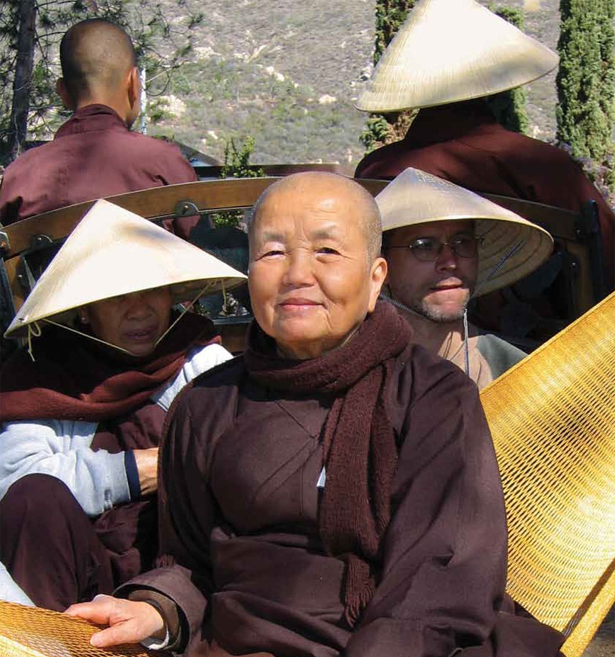 A woman smiles while wearing purple robes and a purple scarf. There are people in the background all wearing purple and pyramid shaped hats.