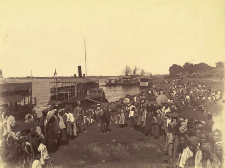 A crowd of people at a riverbank in an old photo.