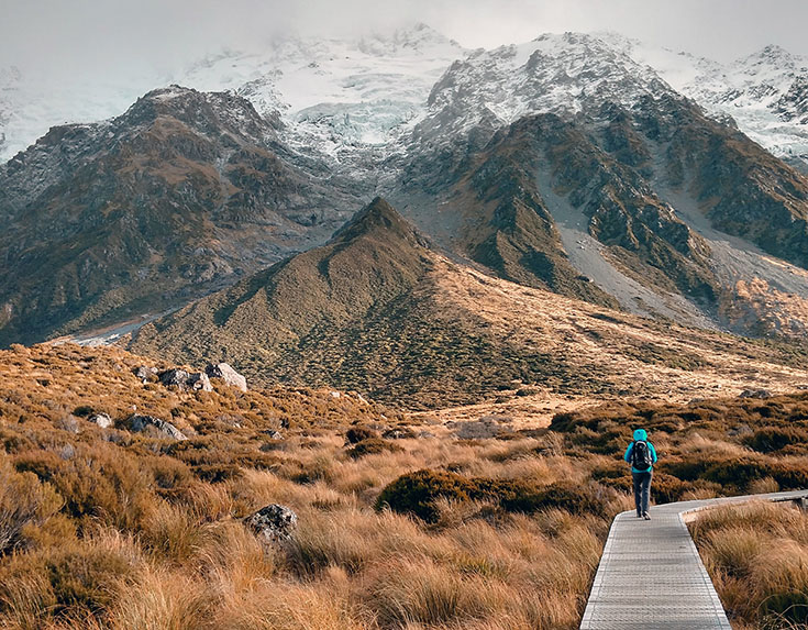 Person walking down a path with mountains in the background.