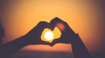 Hands in the shape of a heart around a setting sun