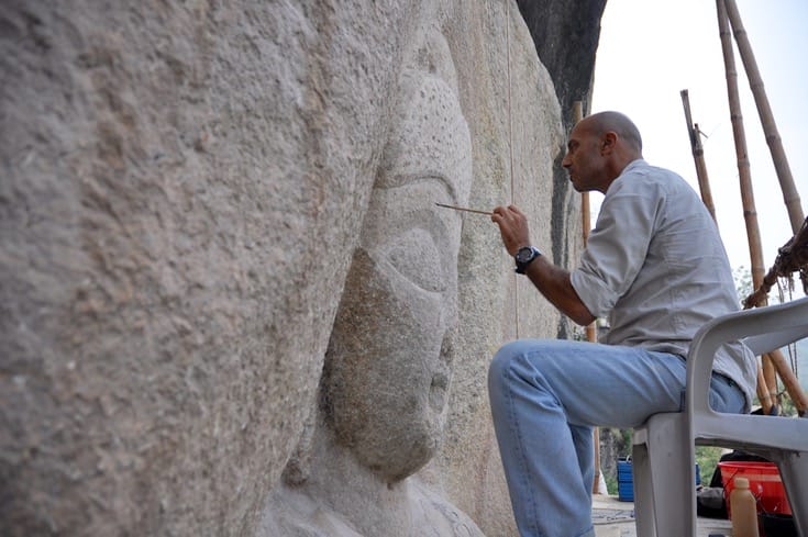 Man restoring the face of a Buddha sculpture.