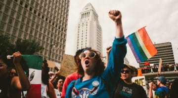 Anti-Trump protestor with Pride Flag in background.