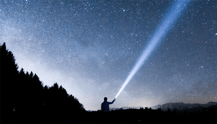 A man with a flashlight in shadow. The flashlight is shining into the sky.