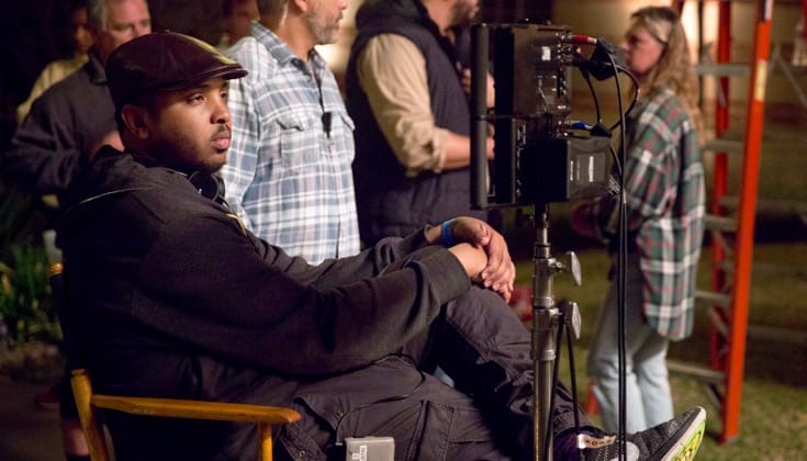 Justin Simien sitting in a director's chair on a studio set.