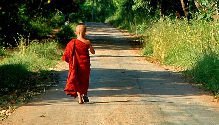 A child in monks robes walking down the road.