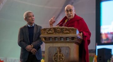 Dalai Lama speaking at lectern with Thupten Jinpa.