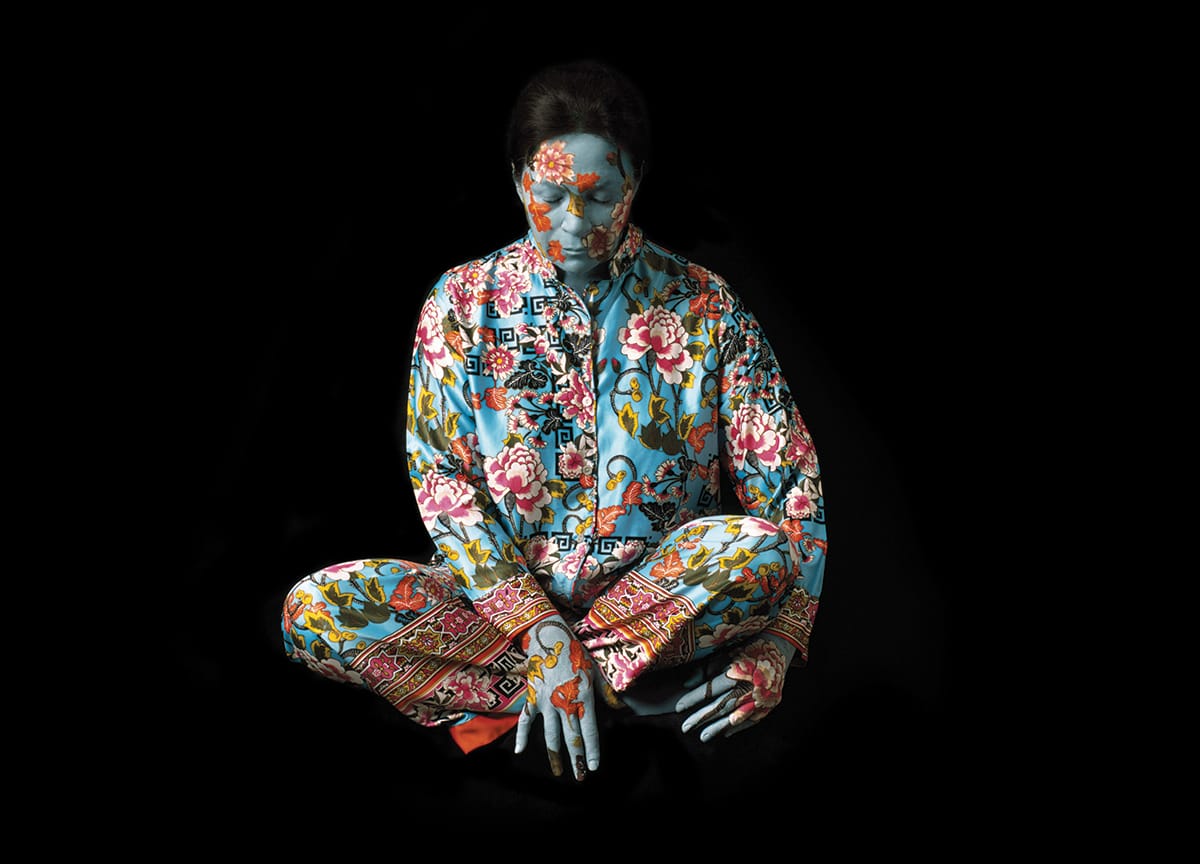 A woman wearing a floral printed silk outfit. Her face is painted like the pattern.