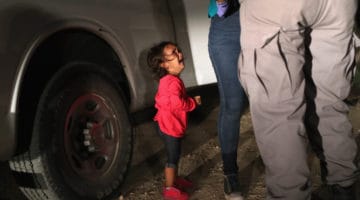 Small girl crying while border guards search her mother.