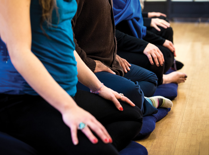 Four people sitting with their legs crossed while meditating.