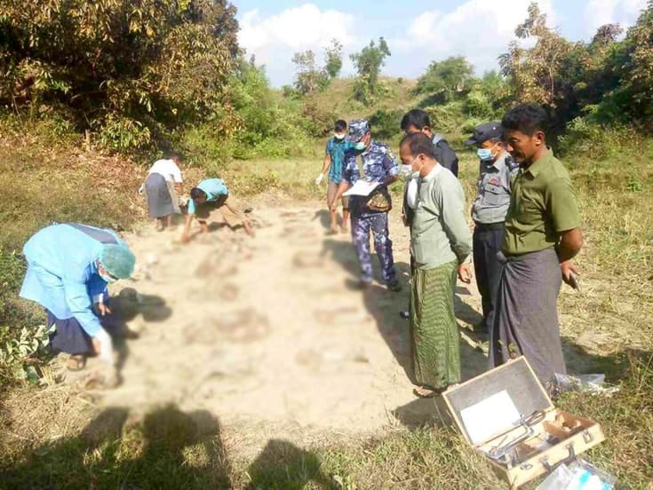 People standing around a mass grave as workers uncover it.