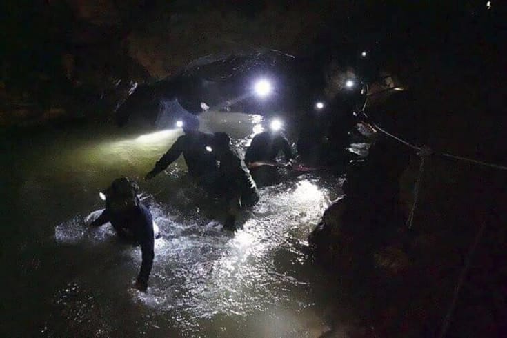 Rescue works wading through a dark, flooded cave wearing headlamps.
