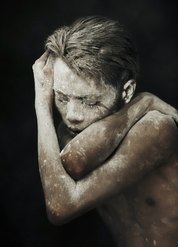 Man wrapping arms around self, with powder on face.
