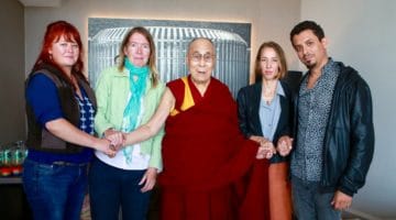 The Dalai Lama holding hands with four others.