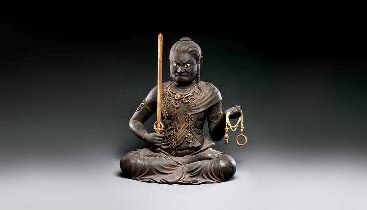 Sculpture of wrathful being Acala, holding a sword and a chain, sitting in meditation posture.