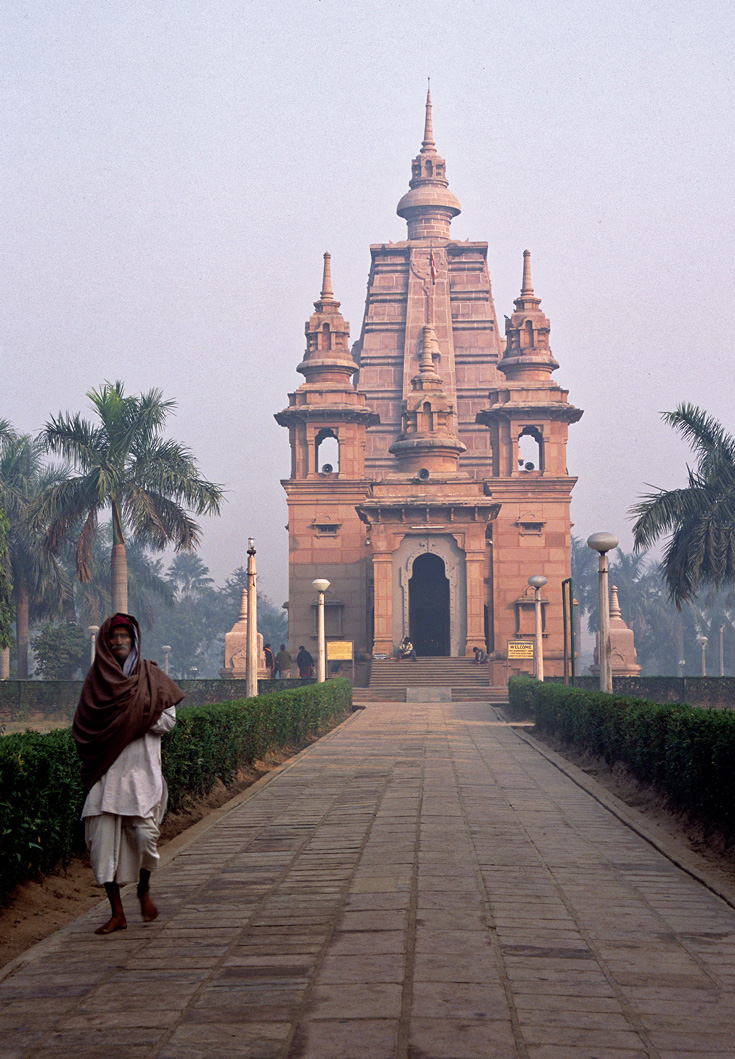 A person walks outside a path near a temple. It is a photo taken at sunset.