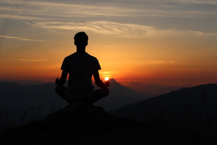 Silhouette of person meditating on mountain
