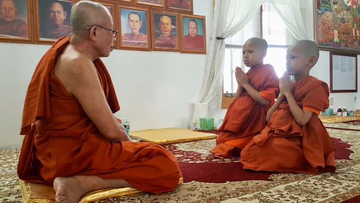 Two boy monks bowing to an elder monk.