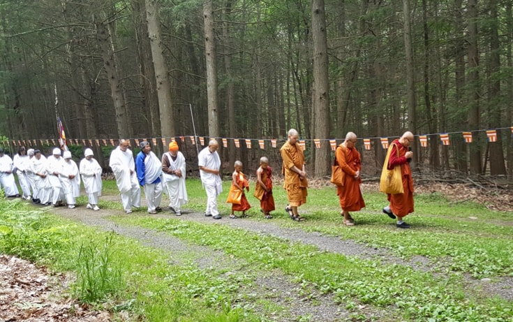 A group of people all walk in a straight line. The people in the left half are all wearing white, and the people on the right are all wearing orange.