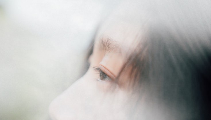 A close up of a side profile of a woman's eye. There is dark hair blowing over the side of her face.