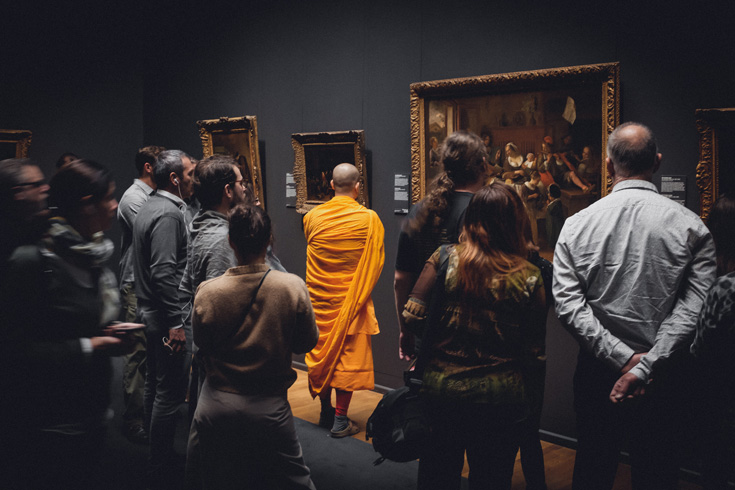 A photo of a bunch of people in an art museum. There is one man dressed in monk's robes.