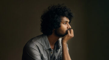 Man with curly hair sits in thought resting his chin in his hand.