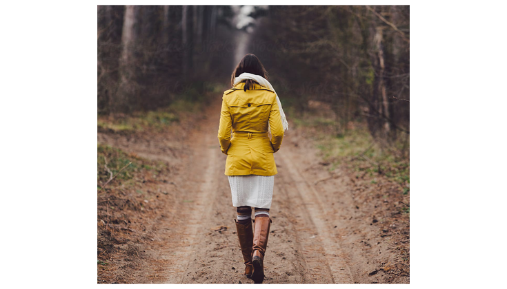 Woman in a yellow jacket walks down a muddy path.