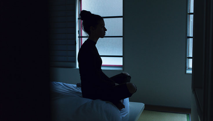 Woman sitting in meditation posture in dark room