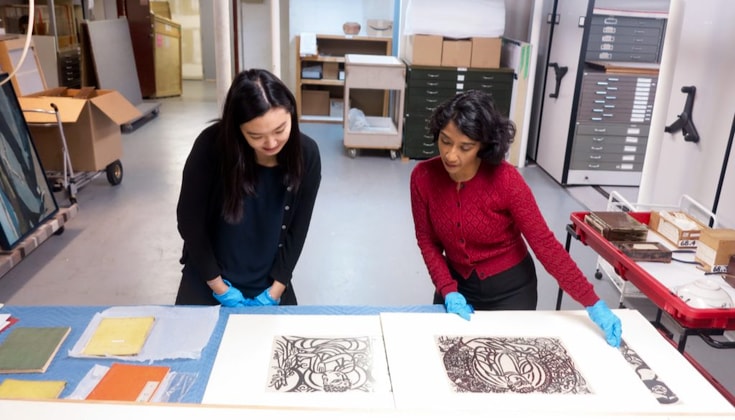 Two women look at art prints in a gallery lab.