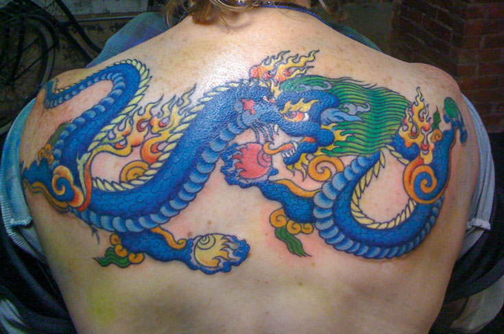 A tattoo of a blue dragon. There is fire coming off the dragon.