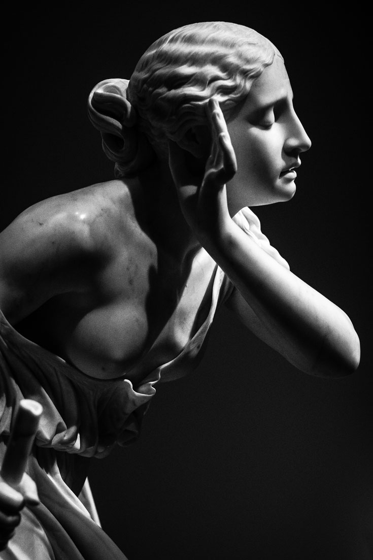 A black and white photo of a marble statue of a woman holding her hand to her ear.