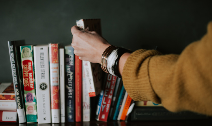 A photo of a person picking a book off of a bookshelf.