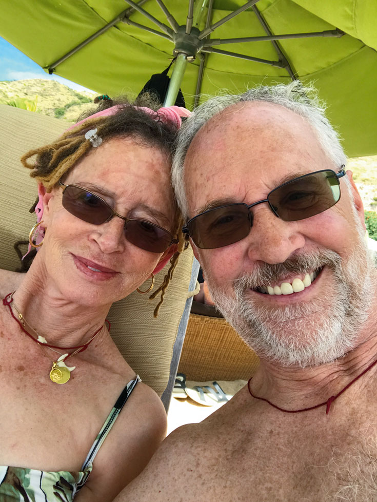 A couple on a beach. There is a green umbrella blocking the sun.