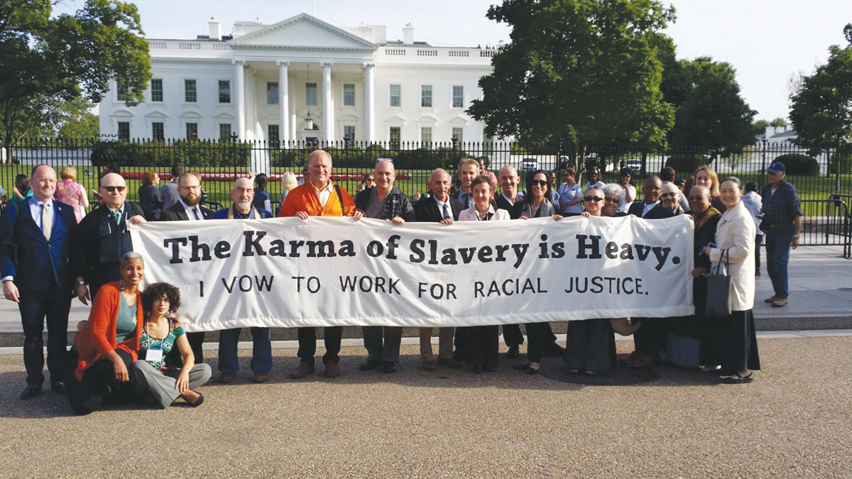 A group of people standing outside the white house with a sign that reads "the karma of slavery is heavy. I vow to work for racial justice."