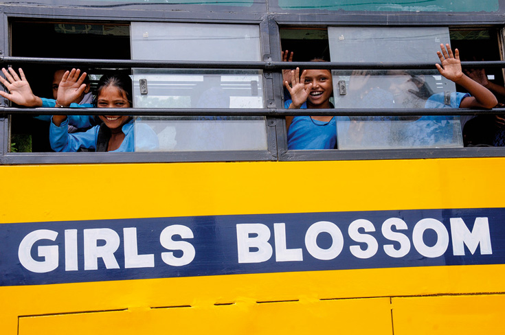 Young girls waving out of a bus that reads "girls blossom"