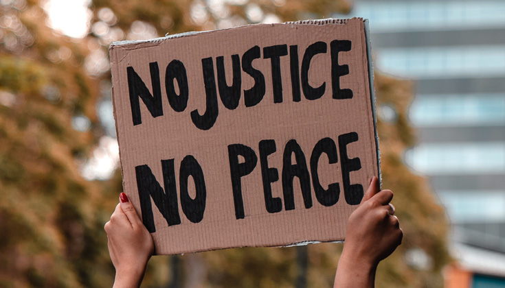 Person holding a cardboard sign that reads "No justice, no peace."