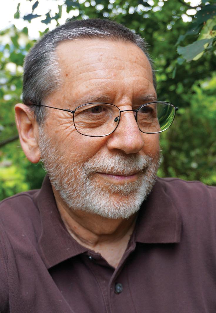 A man smiling with a purple collared shirt on and glasses. 