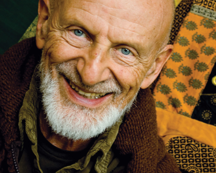 A man smiles while wearing a brown jacket with a green shirt under it.