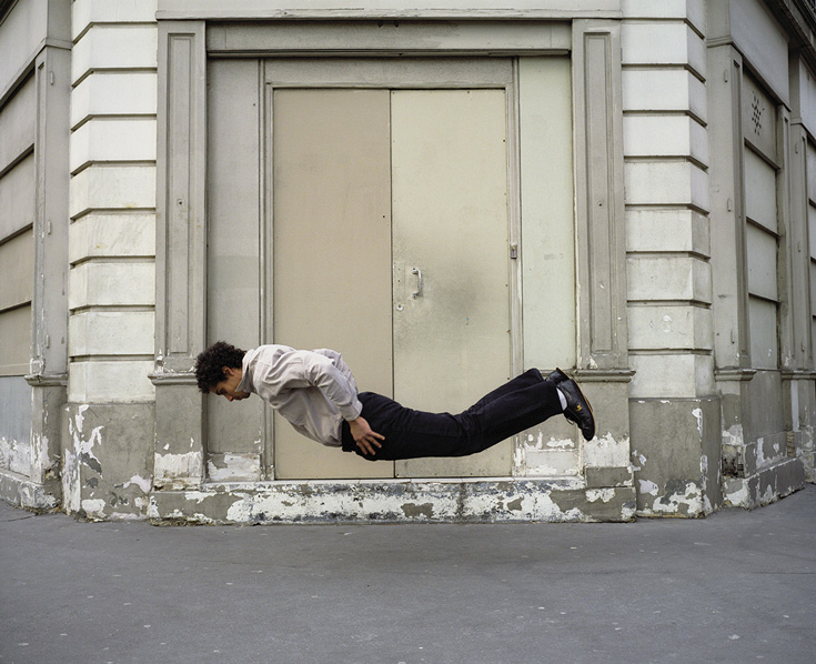 A person laying facedown, a couple of inches above the ground. They are wearing nice clothes.