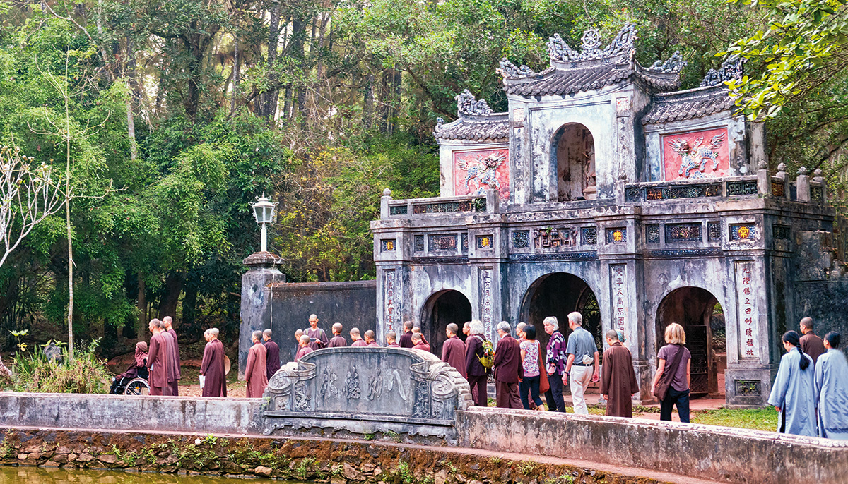 An old fashioned temple. There is a crowd of people in front of it, all wearing maroon robes.