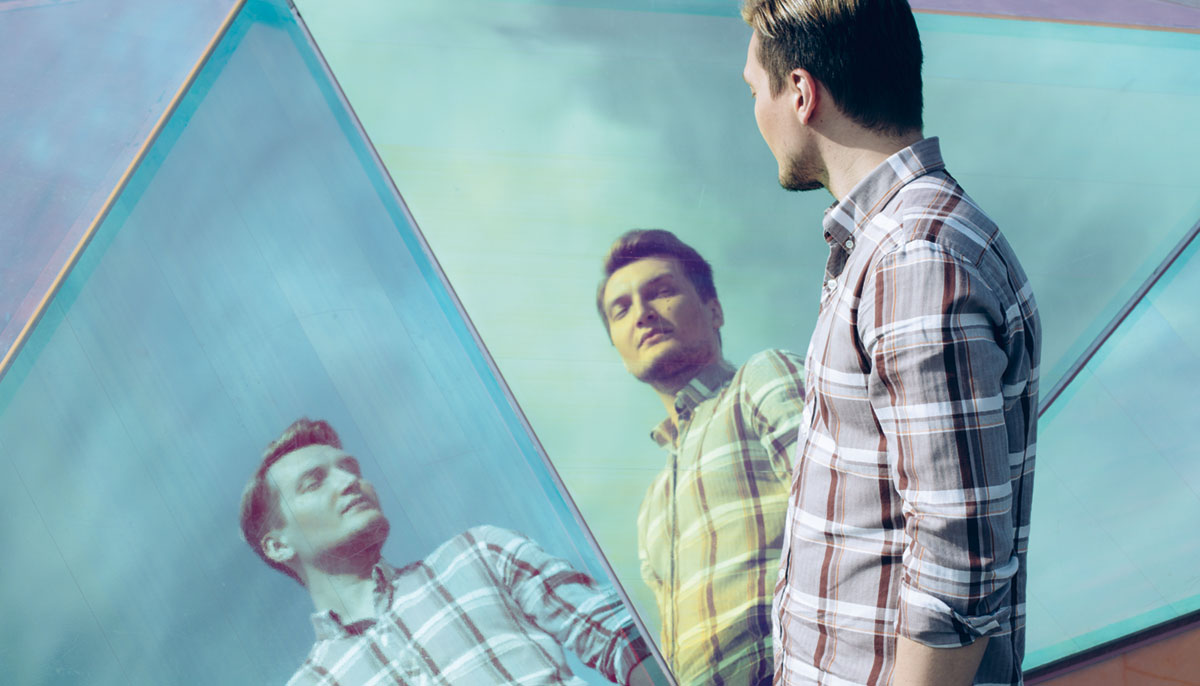 A man looking into a curved mirror in a button up shirt.