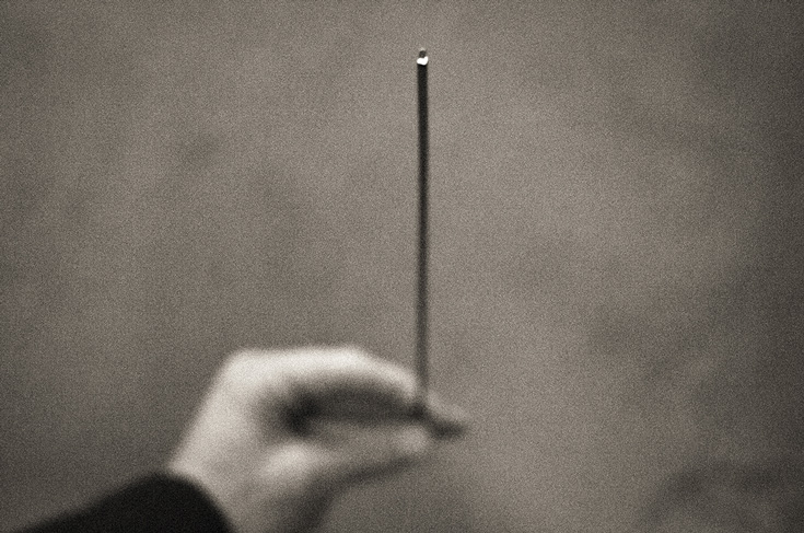 A blurry black and white photo of a hand holding an incense stick.
