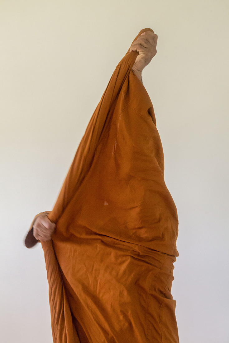 Person putting on orange robes. Only the orange and two hands are visible.