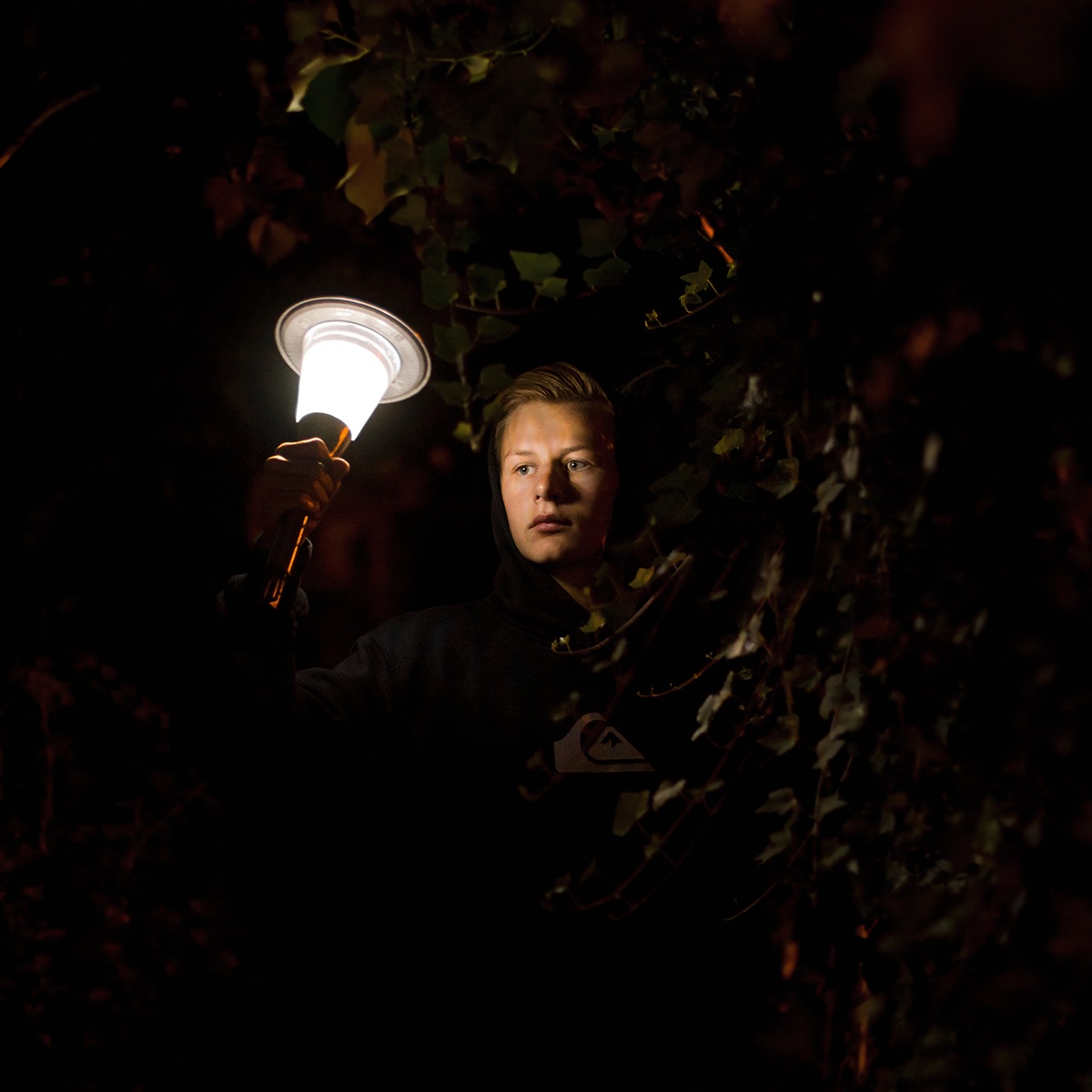A young person holding a lantern. The photo is very dark except for the photo and the face of the person.
