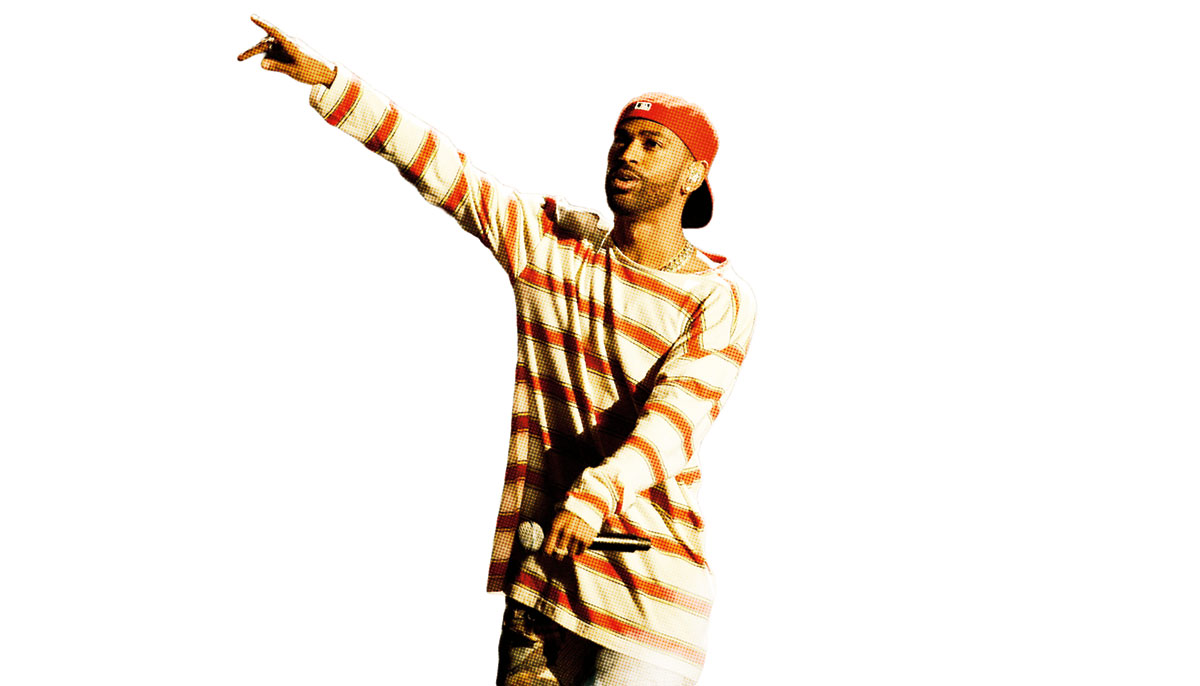 A man pointing wearing a striped shirt and red hat backwards. He is holding a microphone.