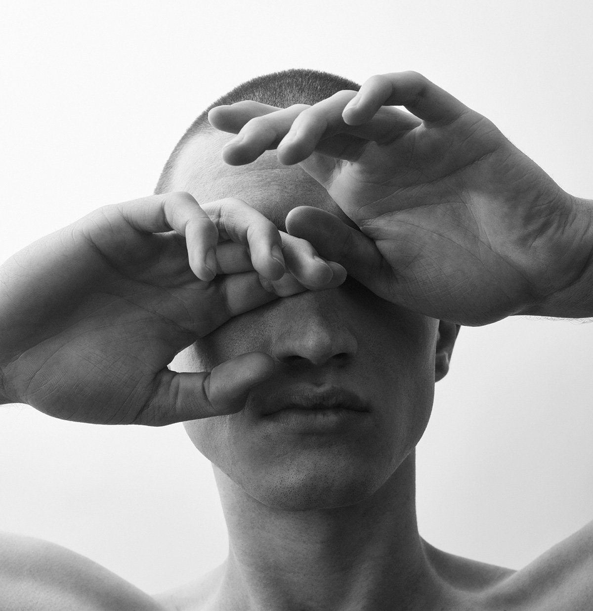 A photo of a person with short hair covering their eyes with their hands.