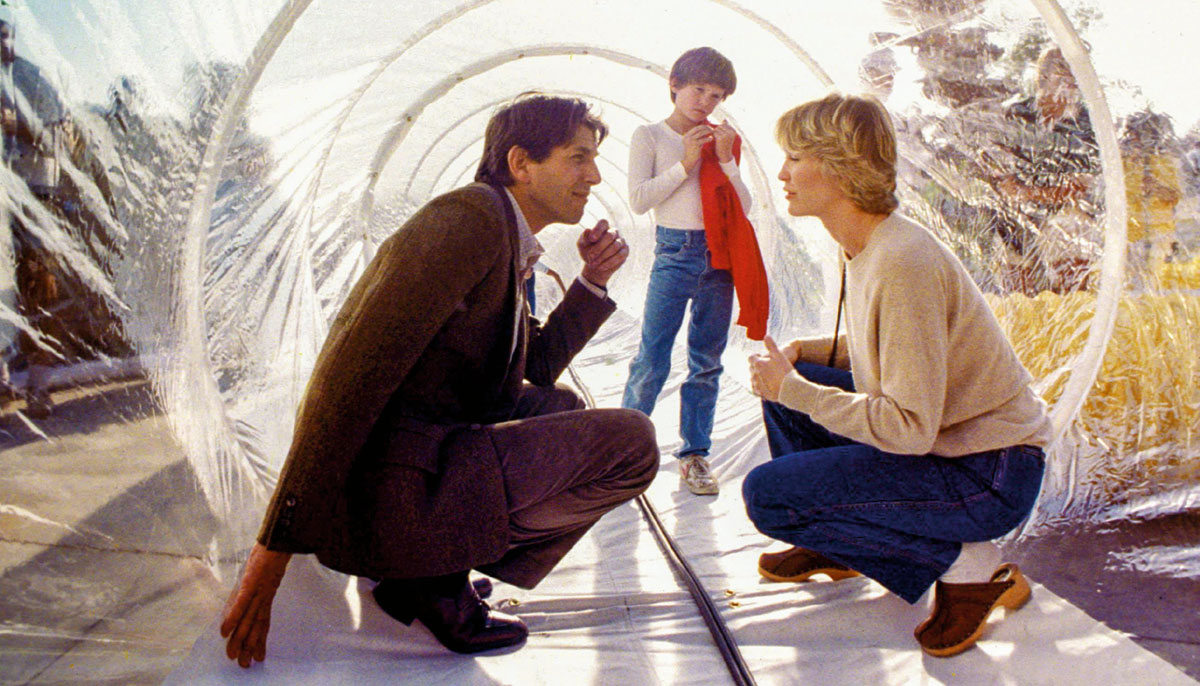 Three people in a plastic tube. A man and woman are crouched and looking at each other and there is a young boy behind them.